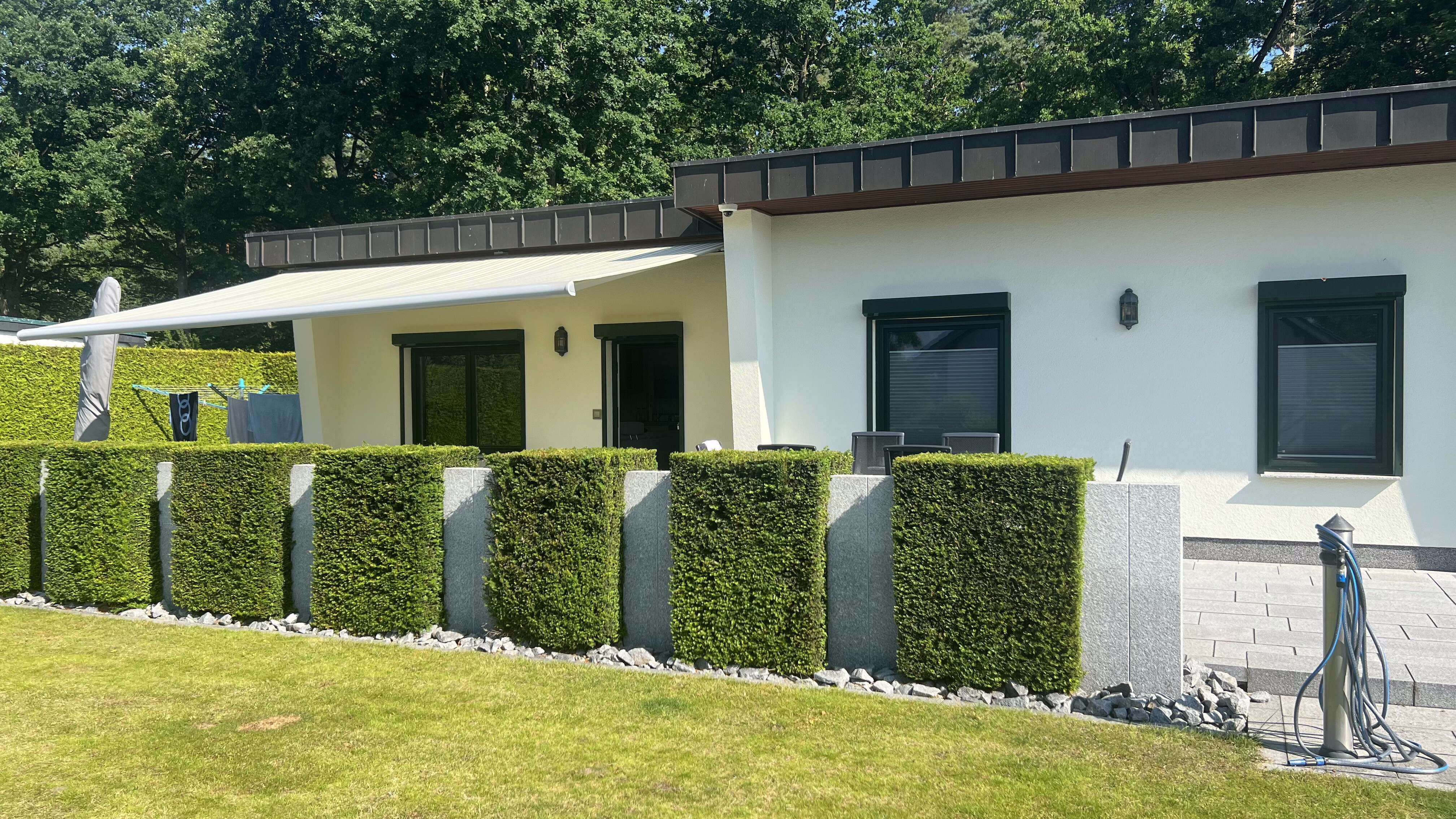 Ferienhaus Kobe von der Gartenseite mit Hecke, Markise und Terrasse