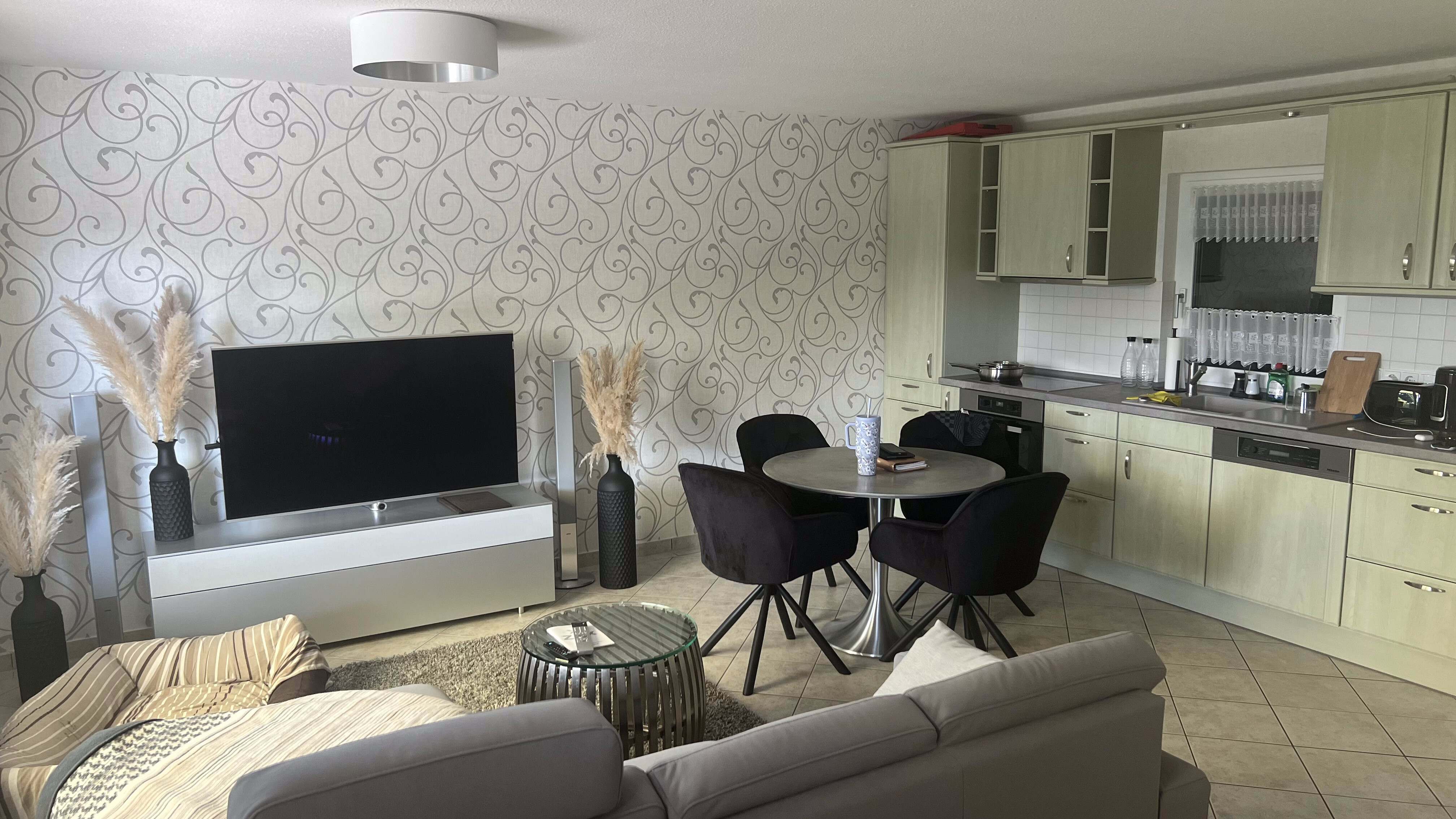 Wohnraum mit Sofa, Smart-TV, Esstisch und offener Küche